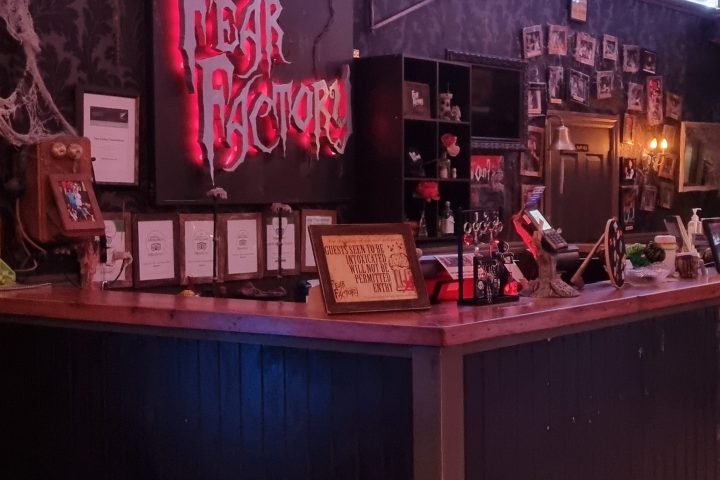 Dimly lit bar with neon 'Fear Factory' sign and various decorations.