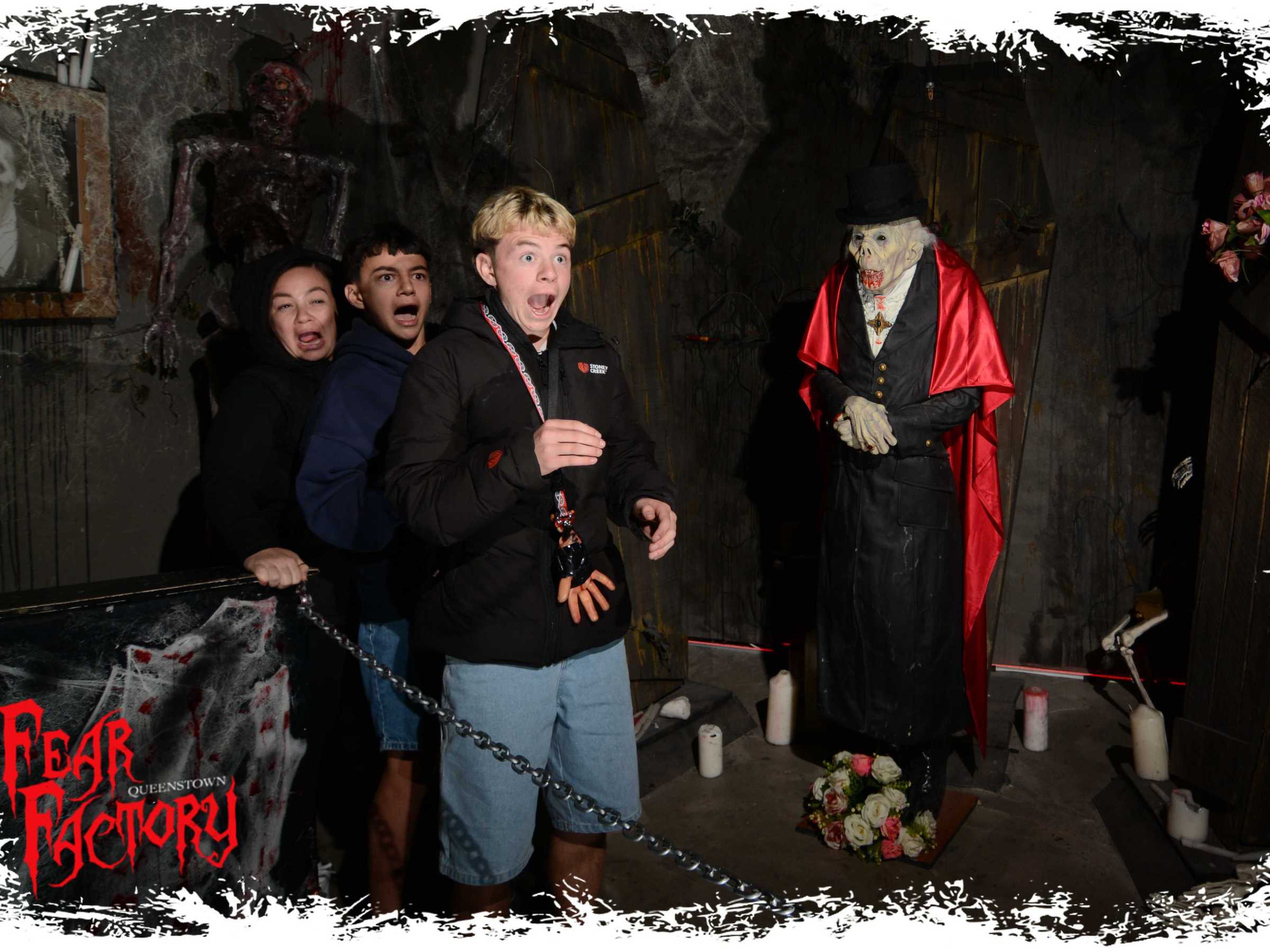 Three people look scared near a vampire statue in a haunted house setting.