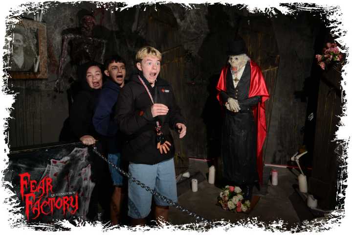 Three people look scared near a vampire statue in a haunted house setting.