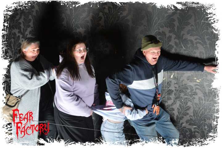 Four people in a haunted house exhibit, looking startled and scared.