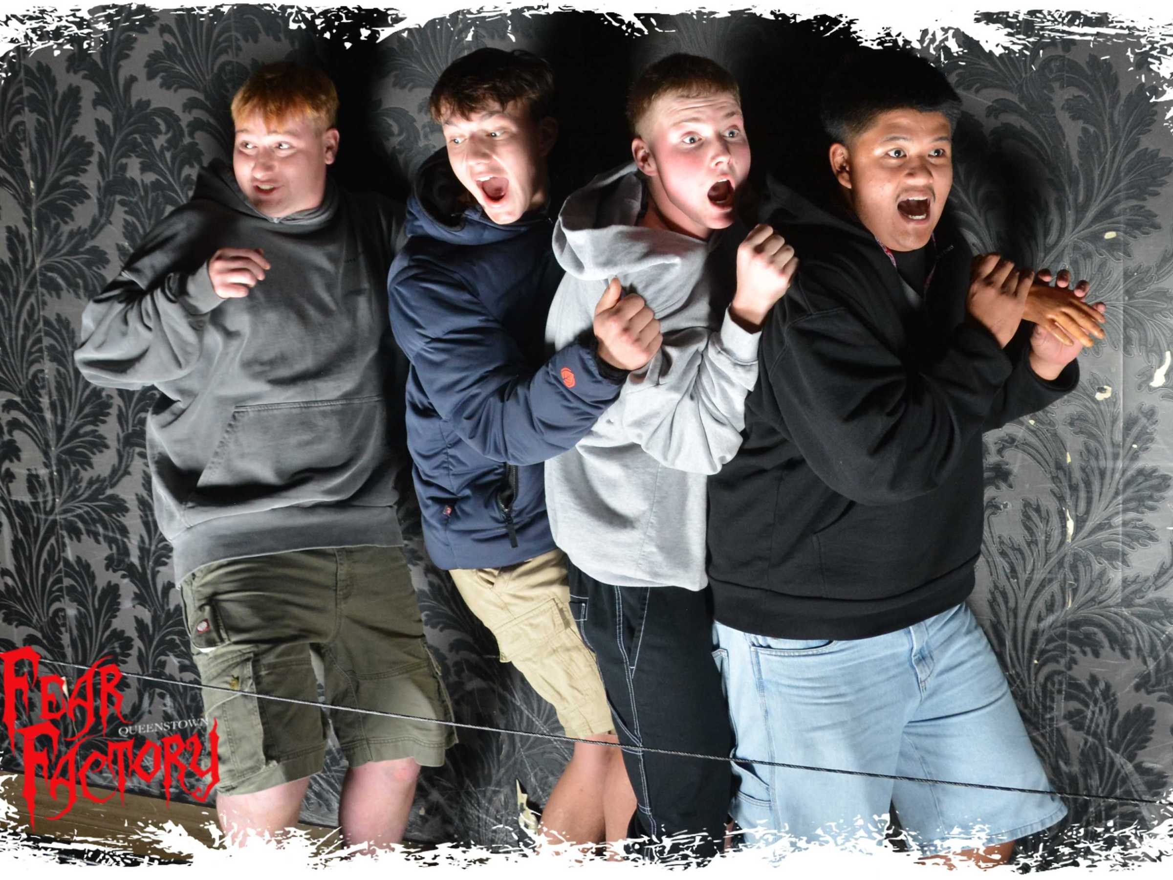 Four people in hoodies and shorts, looking scared against a patterned wall.