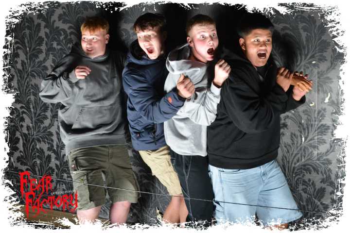 Four people in hoodies and shorts, looking scared against a patterned wall.
