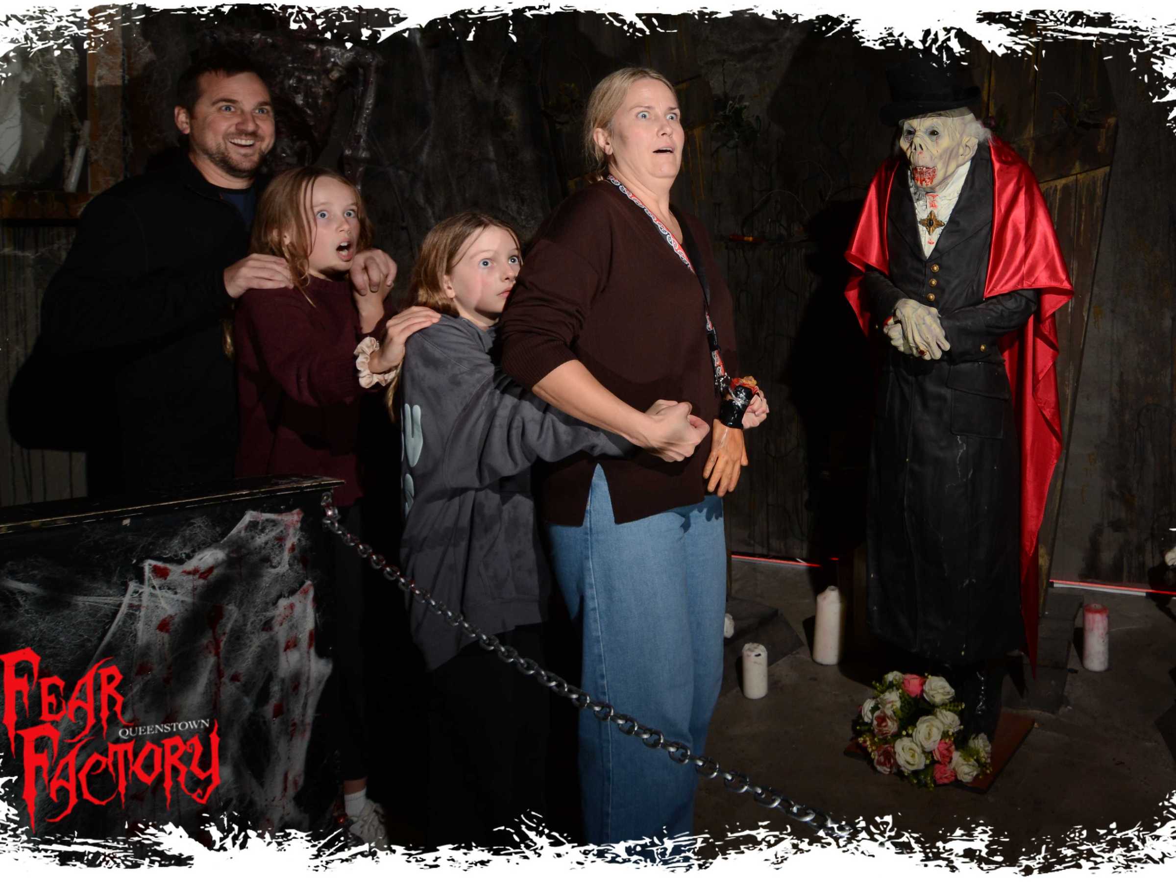 Group posing fearfully beside a skeleton in a vampire costume at a haunted attraction.