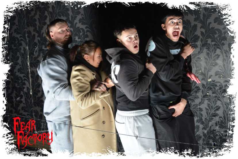 Four people in a haunted house exhibit, looking frightened.