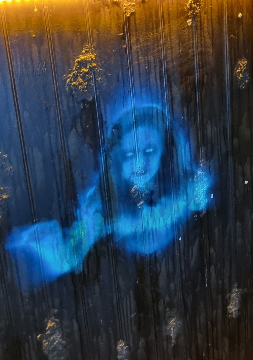 Blue ghostly figure on a dark wall with glowing eyes.